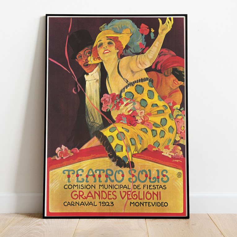 A colorful poster showing a white woman with red hair in a yellow and blue polka dot dress and a white man in a tux, top hat, and monocle with text reading "Teatro Solis, Comision Municipal de Fiestas, Grandes Veglioni, Carnacal 1923, Montevideo." Print is in a black frame, leaning against a white wall.